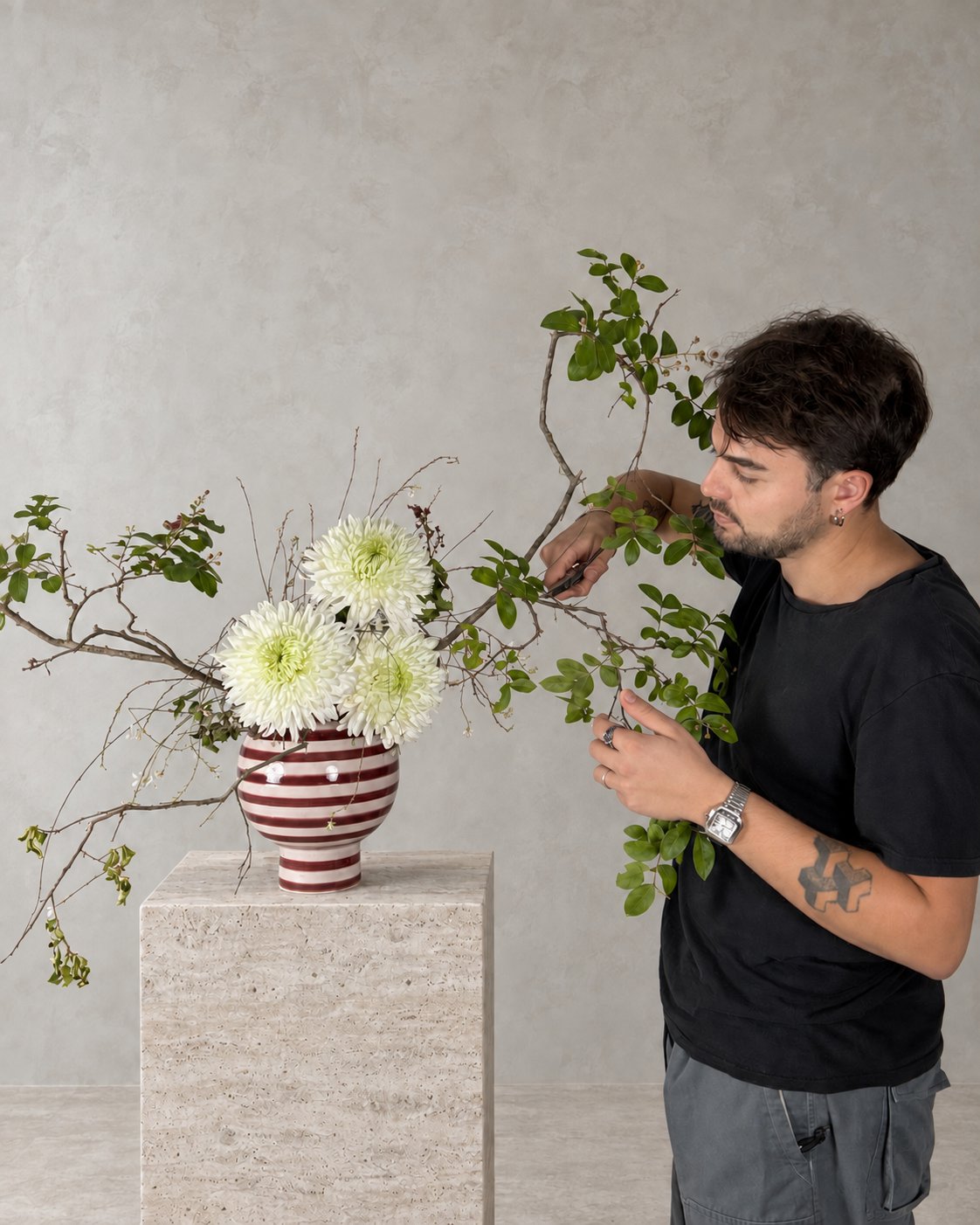 Federico Gasparrini al lavoro nell'atelier, taglia le foglie da un ramo con crisantemi bianchi in un vaso a righe